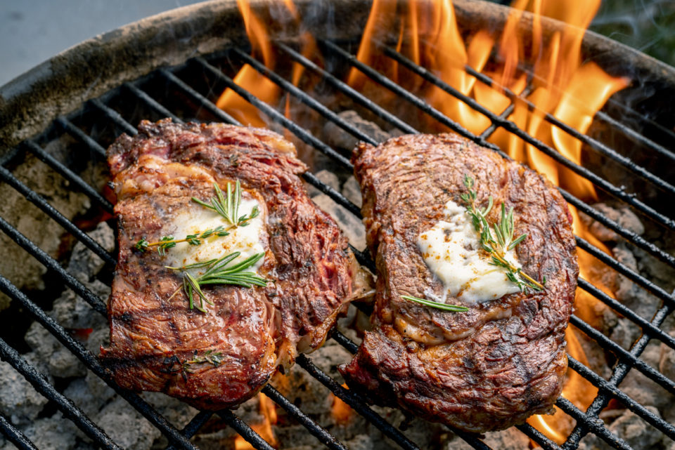 A fiery grill with two juicy ribeye steaks