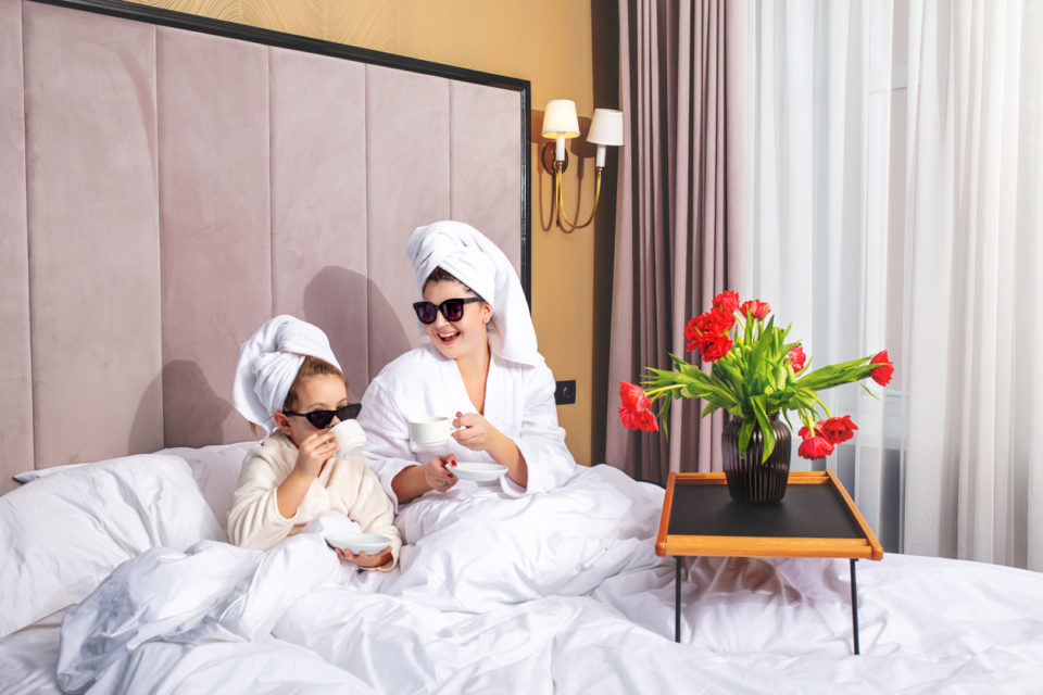 Happy beautiful family mother and daughter in the bedroom on the bed in towels and sunglasses arranged a fashionable tea party