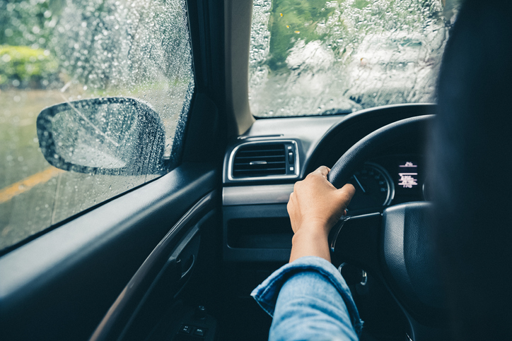 closeup driver's hands on steering wheel driving on rainy day