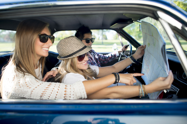 A multi-ethnic group of college age students are taking a road trip together on their spring break. They are looking at a map together.