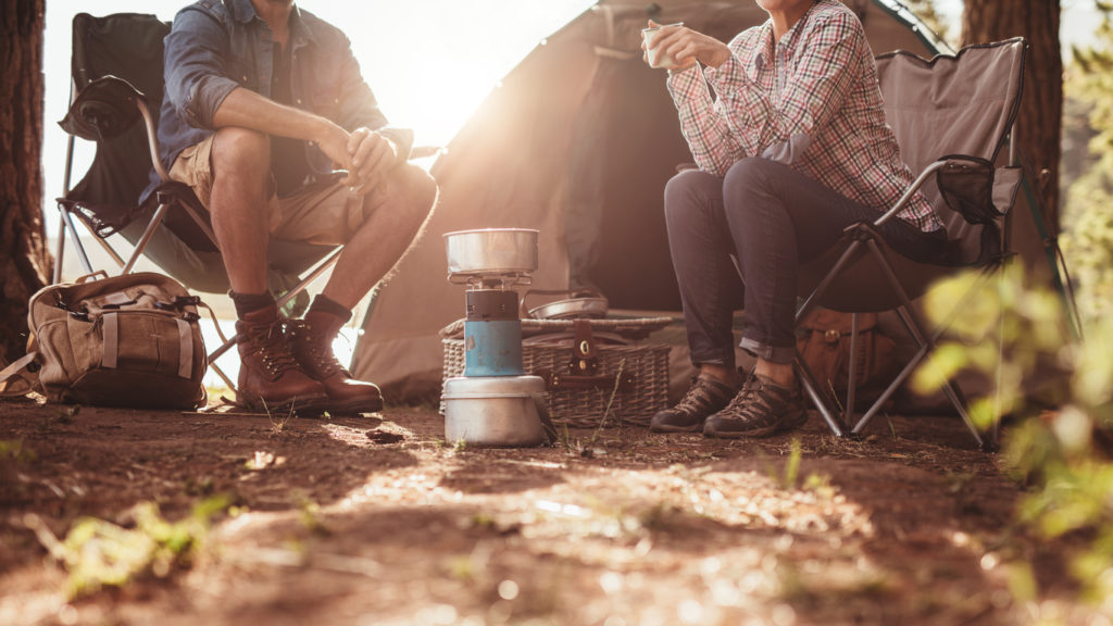 Two people sitting in front of their tents drinking coffee while camping