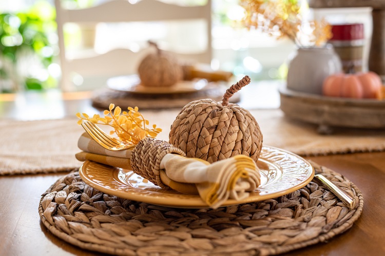 Stylish fall place setting in gold and white with wicker accents in light and bright dining room